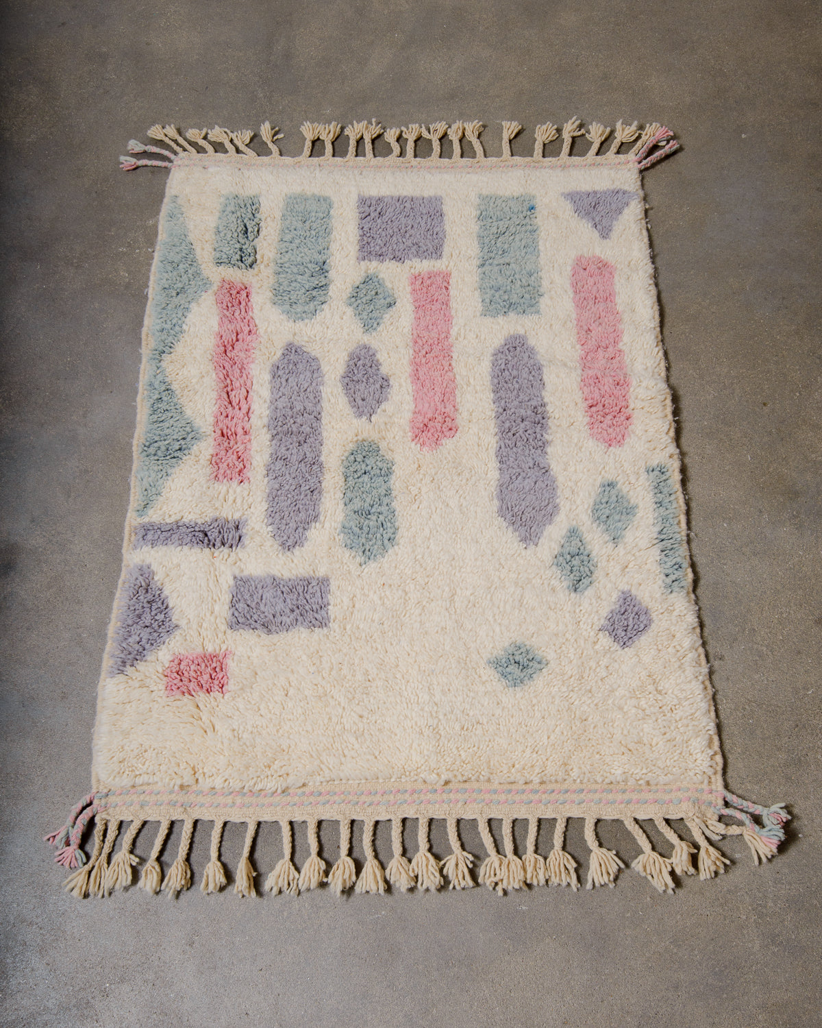 Berberlin Beniourain rug made of cream and pastel coloured wool, laying on concrete studio floor.